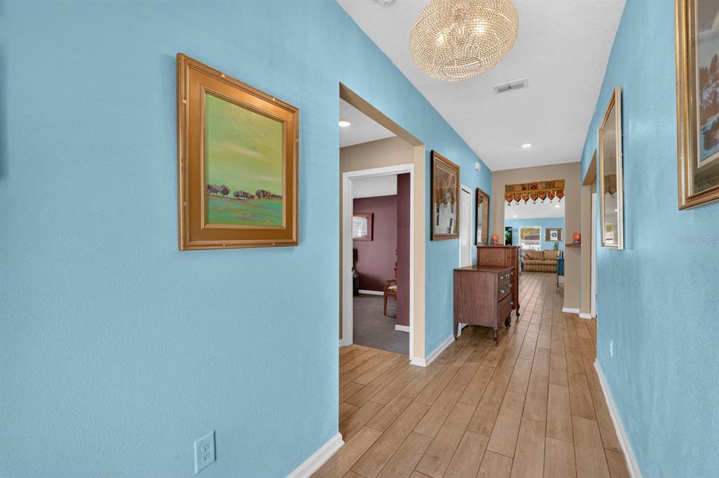 A hallway with light blue walls, wood-look tile flooring, and a decorative crystal chandelier — 81 HICKORY RIDGE ROAD, ST AUGUSTINE, FL