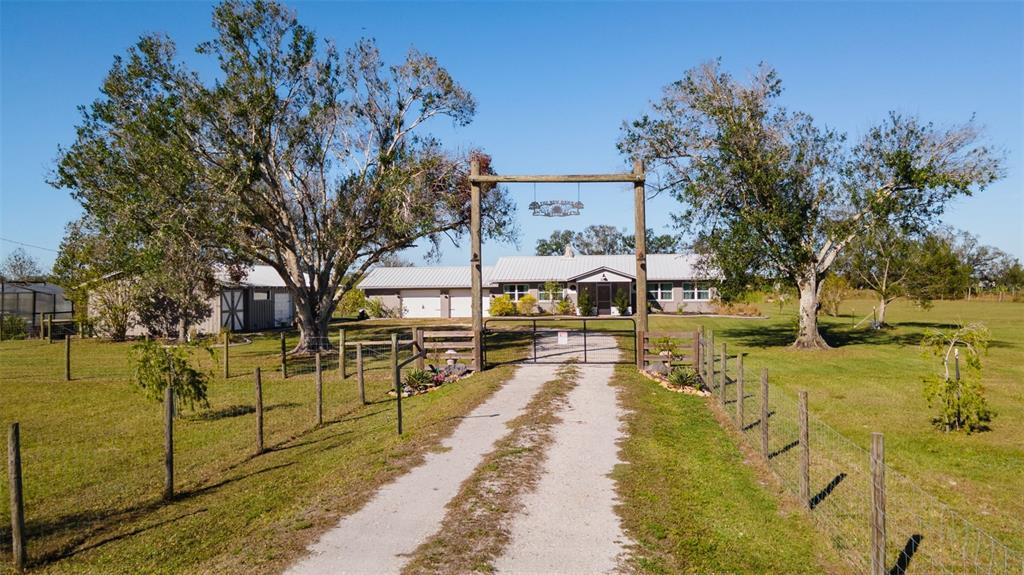 A gravel driveway leads through a gated entrance to a single-story house with trees — 2222 SE MCCLELLAND DRIVE, ARCADIA, FL