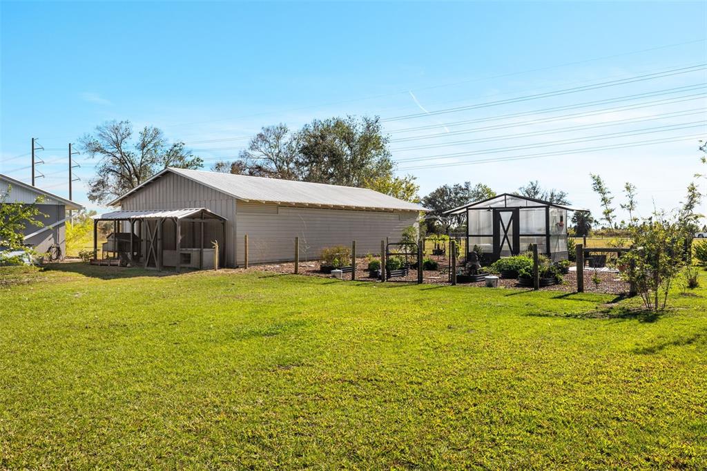 A large metal workshop with an attached coop stands next to a backyard greenhouse — 2222 SE MCCLELLAND DRIVE, ARCADIA, FL