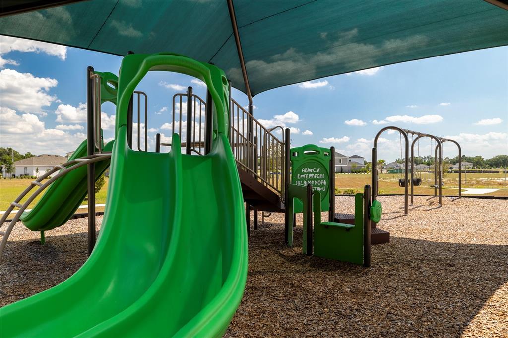 A green playground structure with slides and swings sits under a shade canopy outdoors — 5949 SOPHIEANN STREET, ST CLOUD, FL