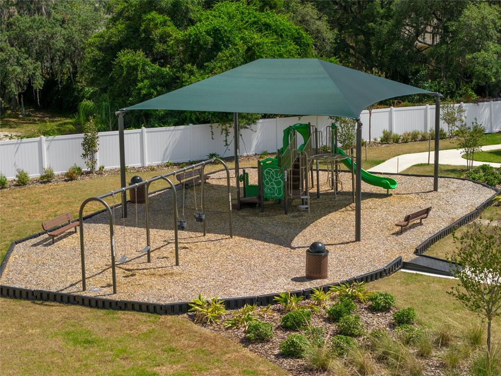 An outdoor playground features a green shade canopy, swing set, and slide on wood chips — 5949 SOPHIEANN STREET, ST CLOUD, FL