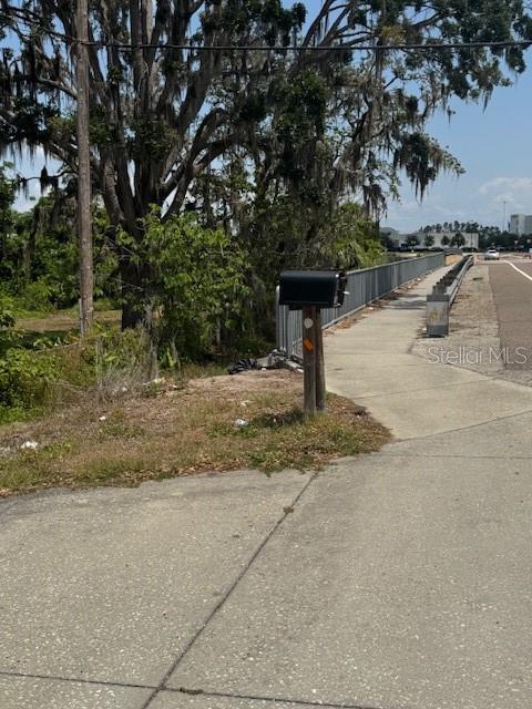 A black mailbox stands on a wooden post beside a sidewalk and metal railing — 10709 E BAY ROAD, GIBSONTON, FL