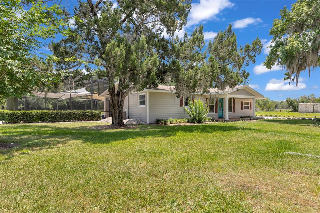 A light-colored house with a screened-in pool area sits on a large, grassy lawn — 4125 RAMBLER AVENUE, ST CLOUD, FL