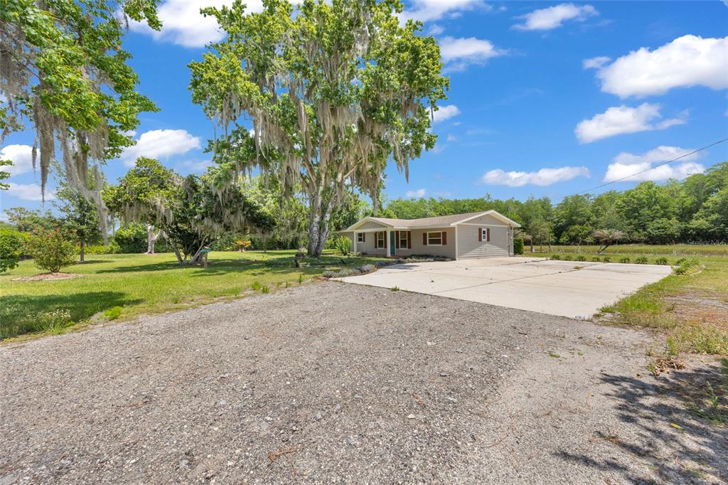 A single-story house with a concrete driveway and large trees in a grassy yard — 4125 RAMBLER AVENUE, ST CLOUD, FL