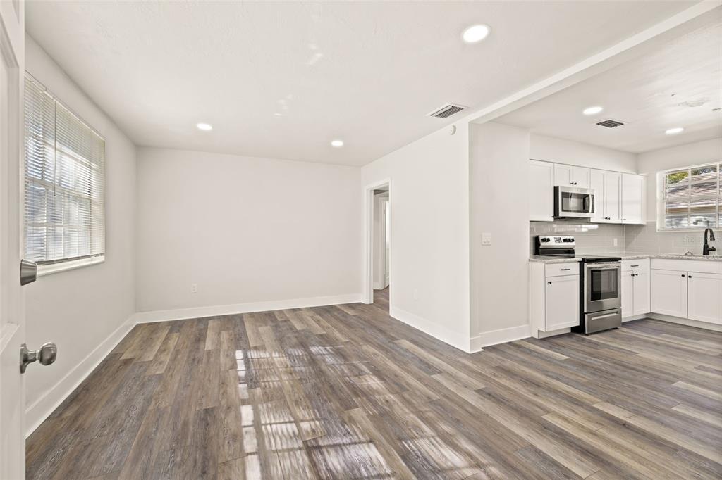 An open-concept dining area with wood-look flooring leads into a white kitchen with stainless appliances — 3817 W BAY TO BAY BOULEVARD, TAMPA, FL