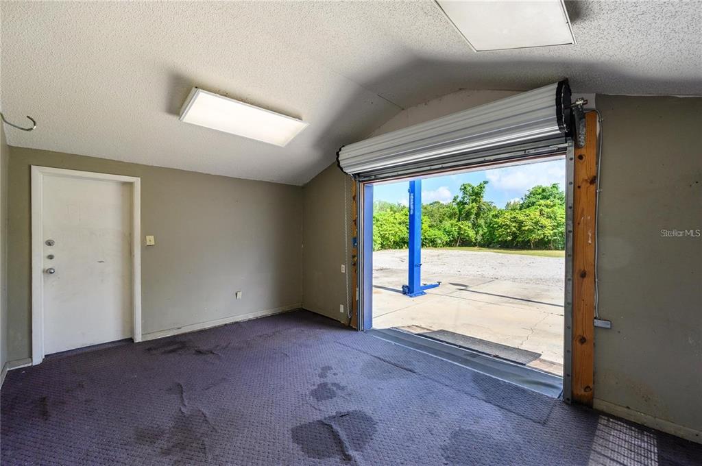 An interior view of a garage with carpeted flooring, a roll-up door, and a car lift — 377 E STATE ROAD 434, LONGWOOD, FL