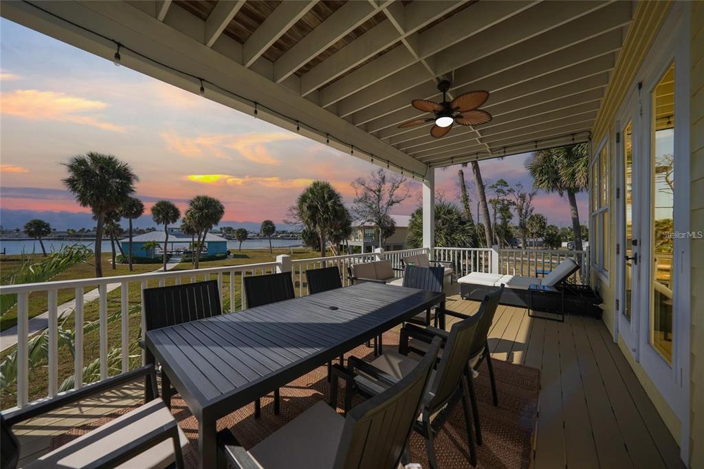 A covered outdoor deck features a dining table, seating, and a ceiling fan overlooking water — 6751 PORTSIDE LANE, ENGLEWOOD, FL
