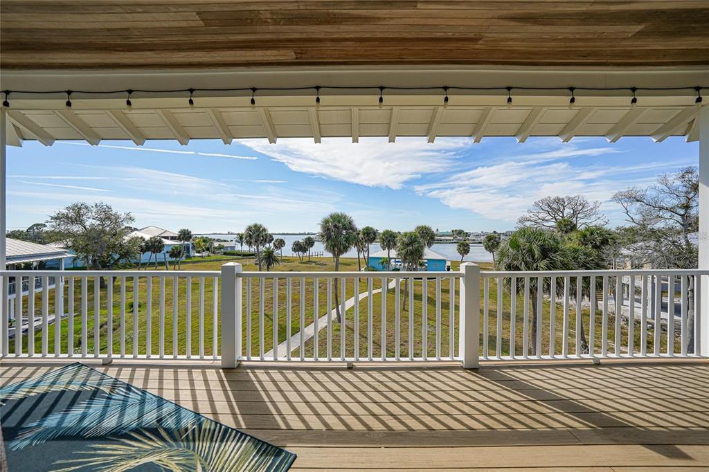 A covered wooden balcony overlooks a grassy yard, palm trees, and a distant body of water — 6751 PORTSIDE LANE, ENGLEWOOD, FL