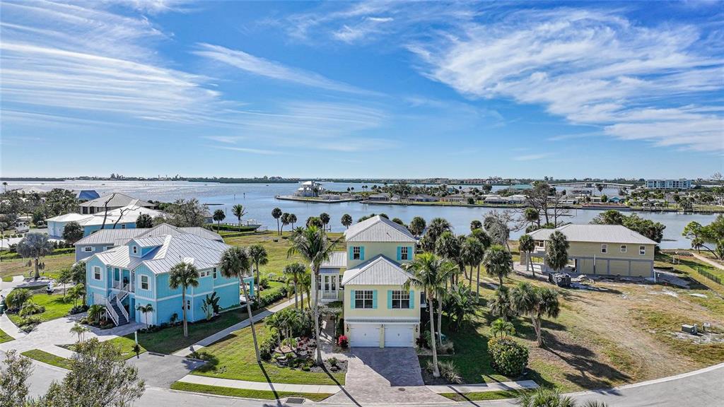 An aerial view shows three coastal-style houses with metal roofs near a waterfront bay — 6751 PORTSIDE LANE, ENGLEWOOD, FL