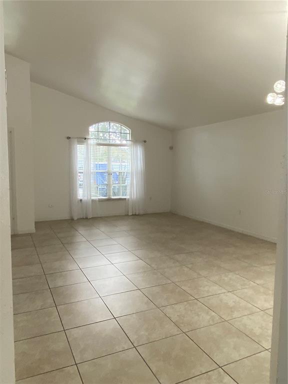 An empty living room features vaulted ceilings, light-colored tile flooring, and a large arched window — 419 BUCKINGHAM CIRCLE, DAVENPORT, FL