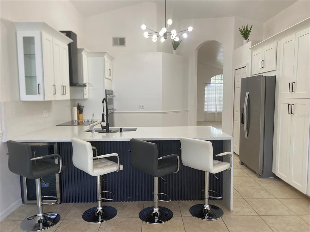 A kitchen features white cabinets, a quartz island with four bar stools, and stainless appliances — 419 BUCKINGHAM CIRCLE, DAVENPORT, FL
