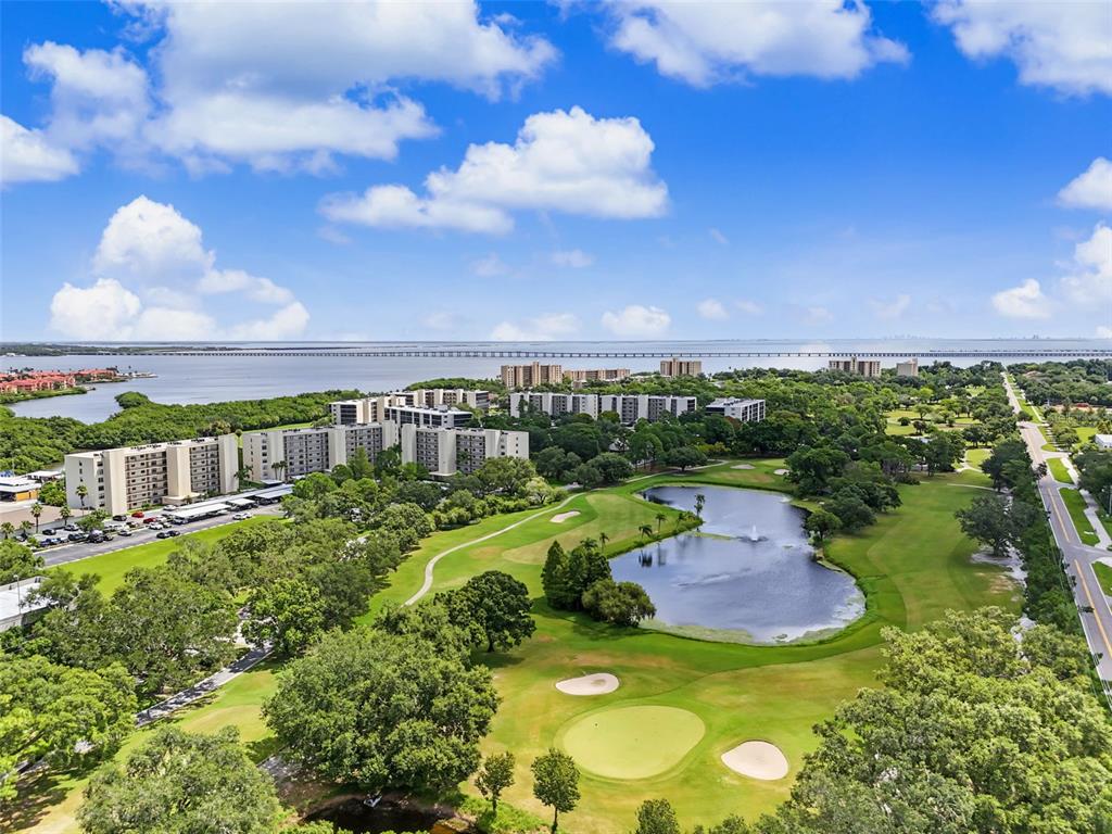 Aerial view of a golf course with a pond, apartment buildings, and a distant bridge — 900 COVE CAY DRIVE UNIT 2B, CLEARWATER, FL