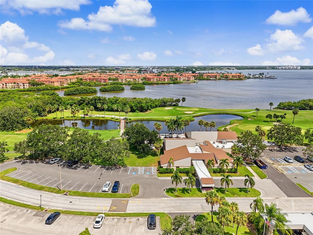 An aerial view shows a clubhouse, parking lot, and golf course beside a large lake — 900 COVE CAY DRIVE UNIT 2B, CLEARWATER, FL