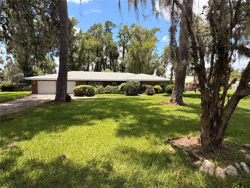 A single-story brick house with a two-car garage sits behind a large grassy lawn — 1940 ALICE DRIVE, ASTOR, FL