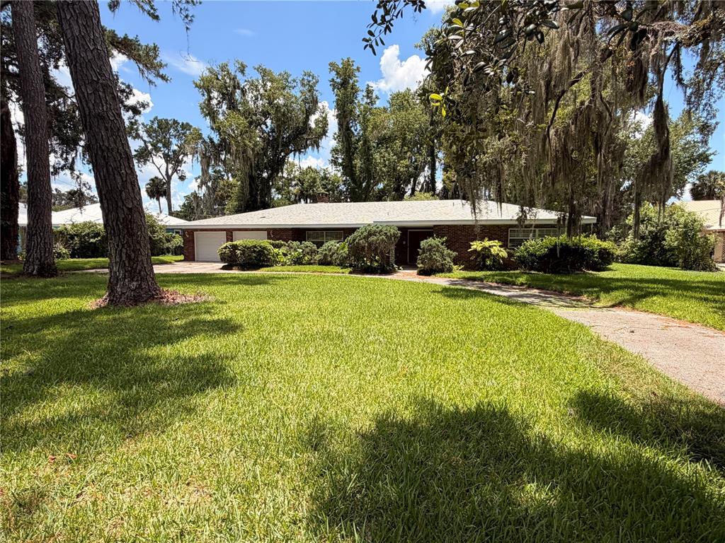 A single-story brick house with a two-car garage sits behind a large grassy lawn — 1940 ALICE DRIVE, ASTOR, FL