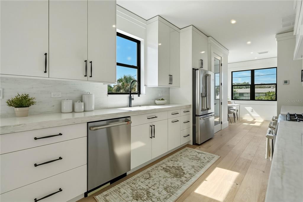 A modern kitchen features white cabinets, stainless steel appliances, marble countertops, and light wood flooring — 205 BATES AVENUE UNIT B, INDIAN ROCKS BEACH, FL