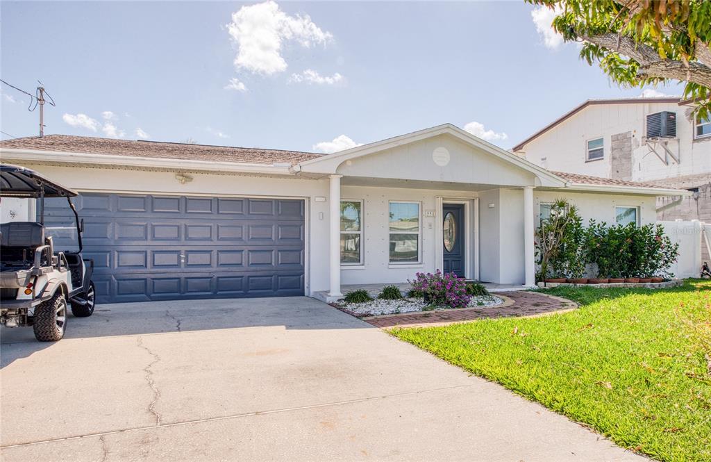 A single-story house with a gray garage door, white exterior, and a paved driveway — 551 CRYSTAL DRIVE, MADEIRA BEACH, FL