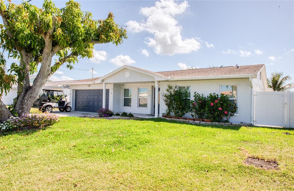 A single-story white house with a dark garage door, a large tree, and a lawn — 551 CRYSTAL DRIVE, MADEIRA BEACH, FL