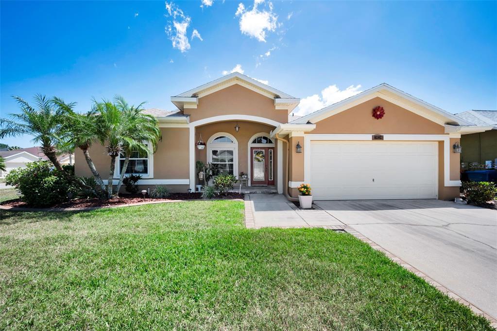 A single-story house with a tan stucco exterior, a two-car garage, and palm trees — 8202 WILD OAKS CIRCLE, LARGO, FL