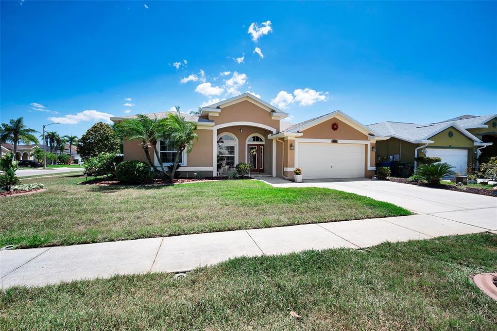 A single-story tan house with a two-car garage and a front walkway under a blue sky — 8202 WILD OAKS CIRCLE, LARGO, FL