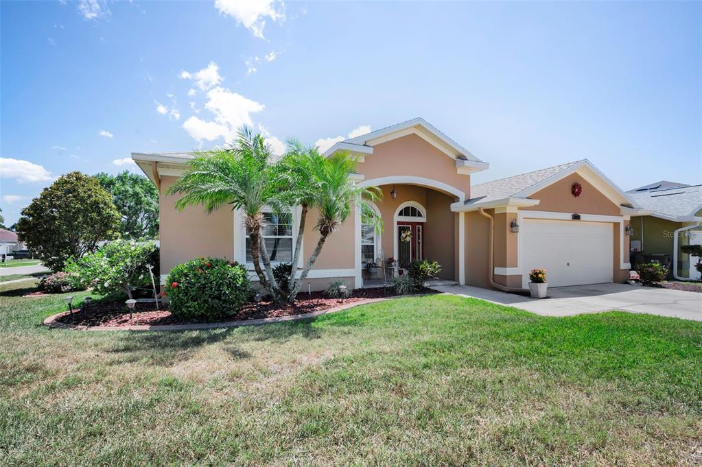 A single-story house with a tan stucco exterior, a two-car garage, and palm trees — 8202 WILD OAKS CIRCLE, LARGO, FL