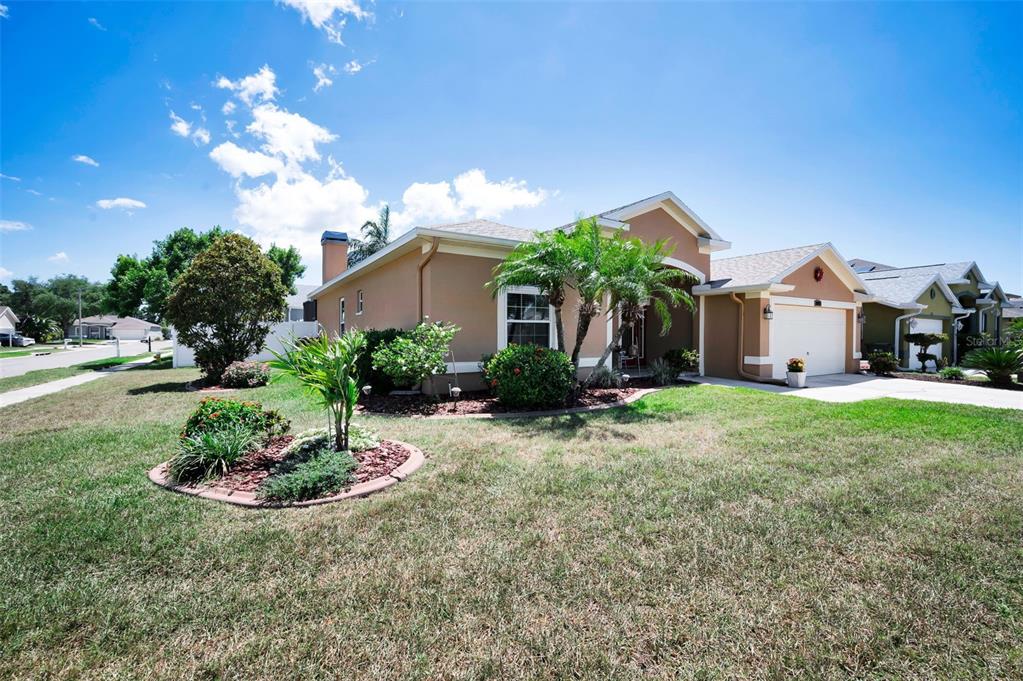 A single-story tan house with a two-car garage and a landscaped front yard — 8202 WILD OAKS CIRCLE, LARGO, FL