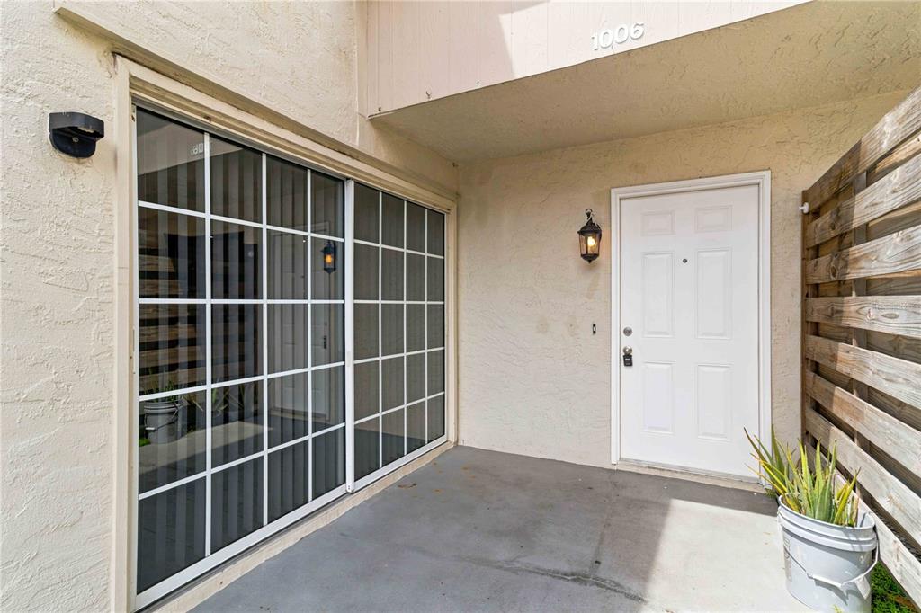 A concrete entryway features a white front door, a sliding glass door, and a potted plant — 1006 LONGFELLOW COURT, SARASOTA, FL