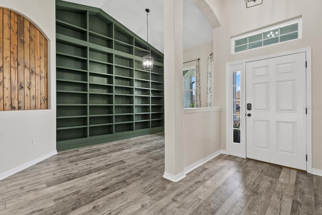 An entryway features wood-look flooring, a large green built-in bookshelf, and a white front door — 12211 23RD STREET E, PARRISH, FL