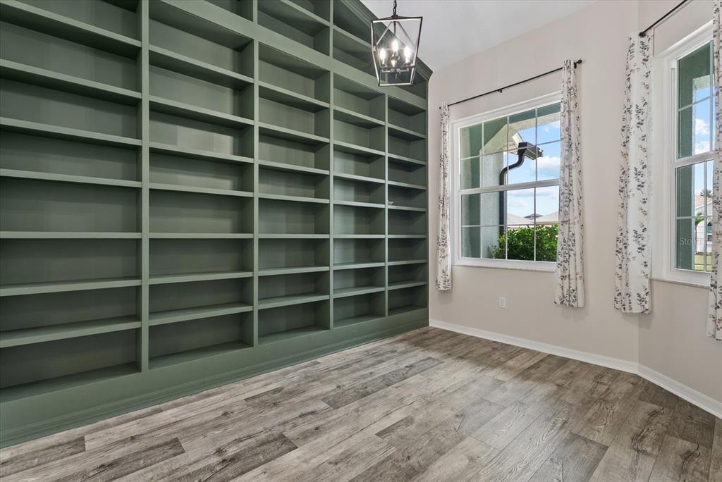 A room features a large, sage green built-in bookshelf, wood-look flooring, and two windows with curtains — 12211 23RD STREET E, PARRISH, FL