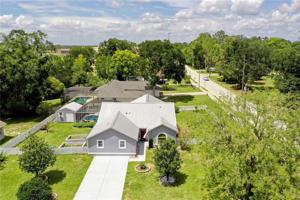 An aerial view of a gray house with a metal roof, driveway, and backyard pool — 1050 FAHNSTOCK STREET, EUSTIS, FL
