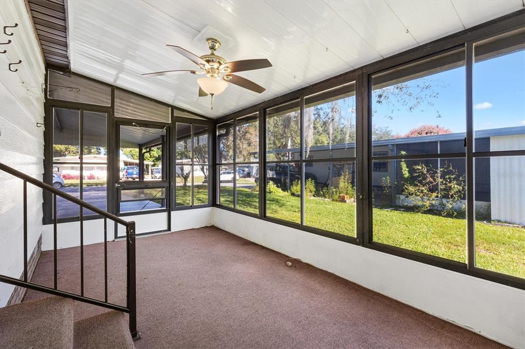 A sunroom with brown carpet, a ceiling fan, and large windows overlooking a grassy yard — 732 ROYAL PALM AVENUE, THE VILLAGES, FL