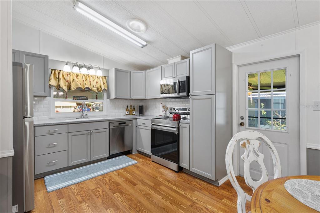 A kitchen features gray cabinets, stainless steel appliances, white subway tile backsplash, and wood flooring — 732 ROYAL PALM AVENUE, THE VILLAGES, FL
