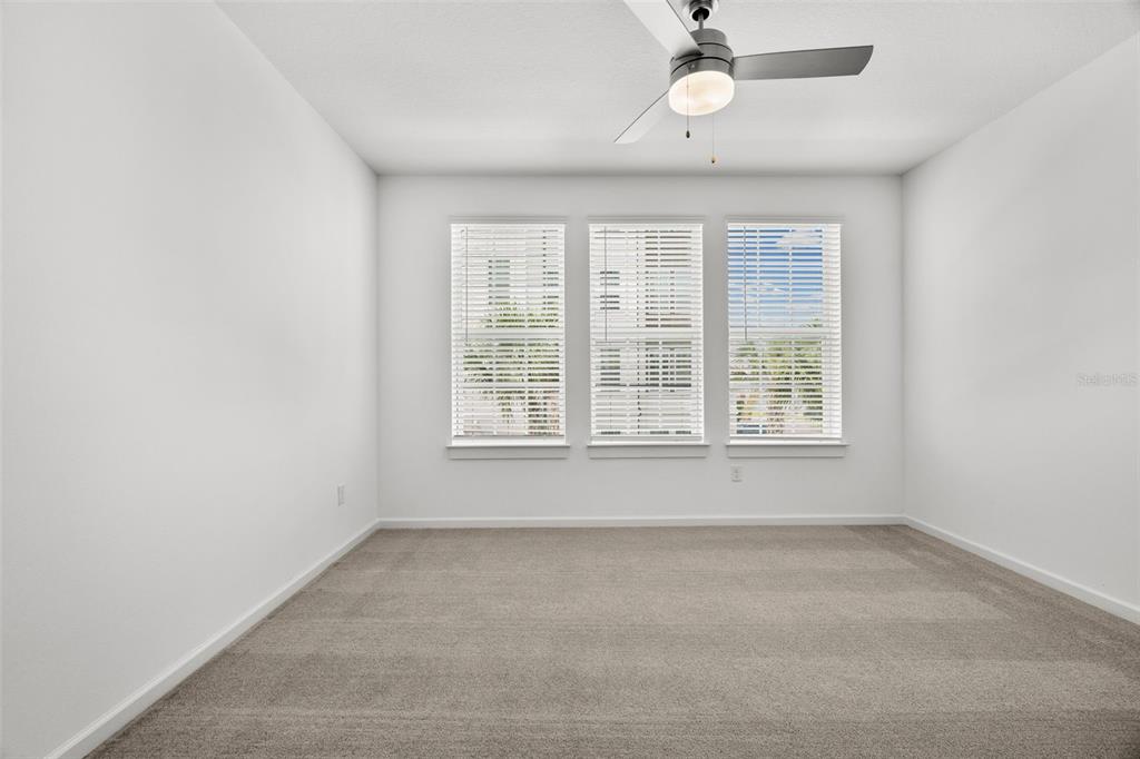 A bright, empty bedroom features white walls, beige carpeting, a ceiling fan, and three windows — 1700 RANCH ROAD UNIT B3-6315, NOKOMIS, FL