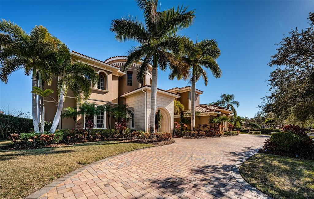 A two-story stucco house with a stone entryway and palm trees sits behind a paver driveway — 9209 SILVERTHORN ROAD, SEMINOLE, FL
