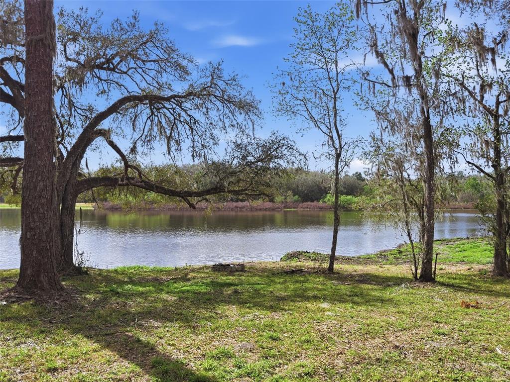 A grassy yard with large trees overlooks a calm lake under a blue sky — 0 DEEPWELL DRIVE, BROOKSVILLE, FL