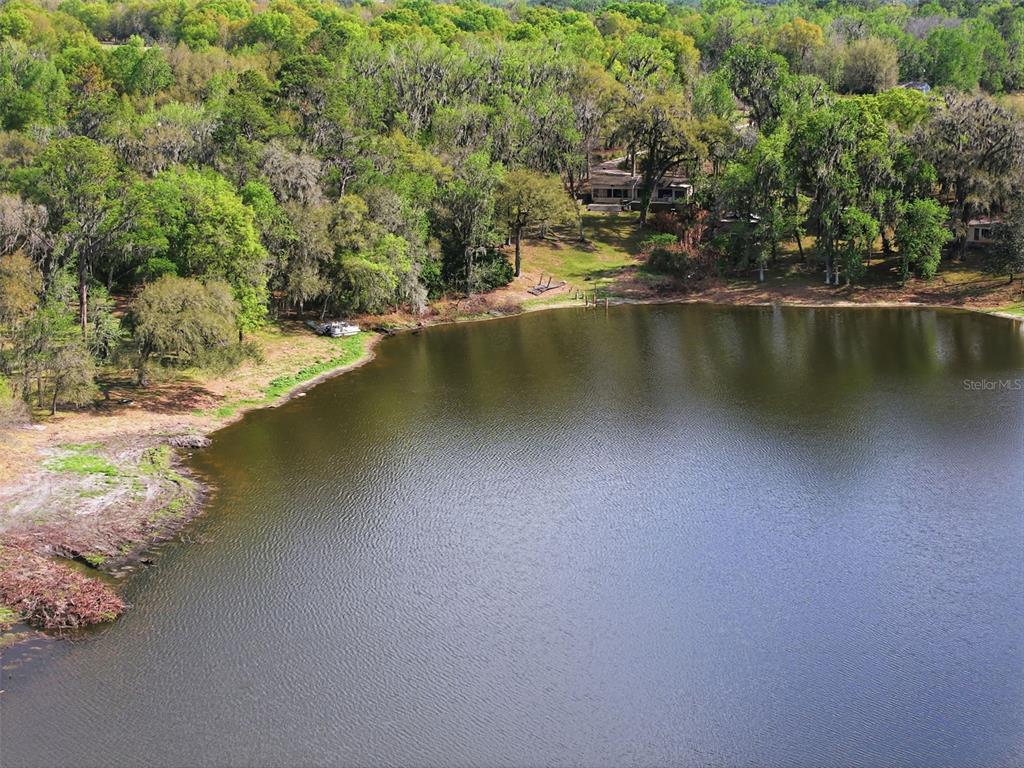 An aerial view shows a house nestled in a wooded area beside a large lake — 0 DEEPWELL DRIVE, BROOKSVILLE, FL