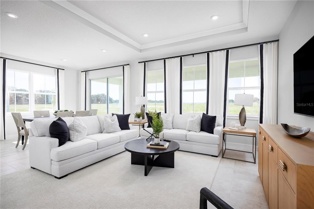 A bright living room features white sofas, a round coffee table, and large windows — 22145 PINE GROVE LOOP, LEESBURG, FL