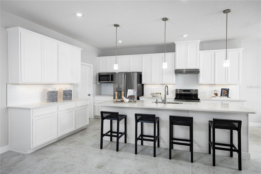 A modern kitchen features white cabinetry, a large island with four black stools, and stainless appliances — 22145 PINE GROVE LOOP, LEESBURG, FL