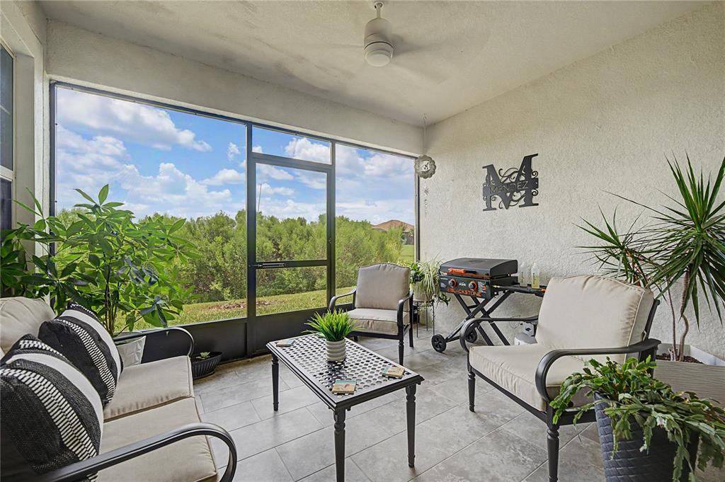 A screened-in patio features tile flooring, outdoor furniture, a grill, and a view of greenery — 10228 ECHO DOCK LOOP, SAN ANTONIO, FL