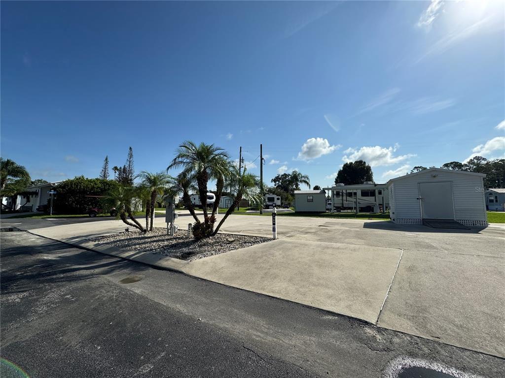 A paved lot features a small palm tree island and a white storage shed — 1389 SHIPWRECK LANE, ST CLOUD, FL