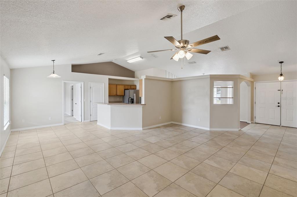 A spacious living room with tile flooring, a vaulted ceiling, and an open kitchen area — 11434 PATRICO LOOP, CLERMONT, FL