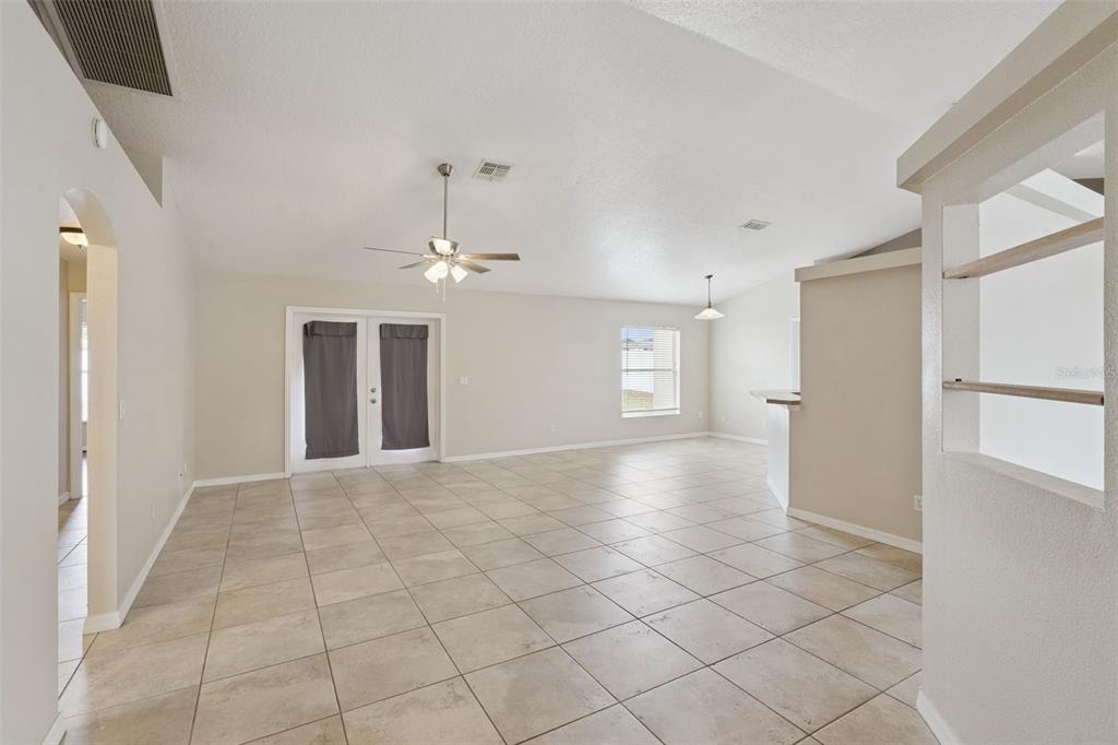 A spacious living room features light tile flooring, a ceiling fan, and glass patio doors — 11434 PATRICO LOOP, CLERMONT, FL