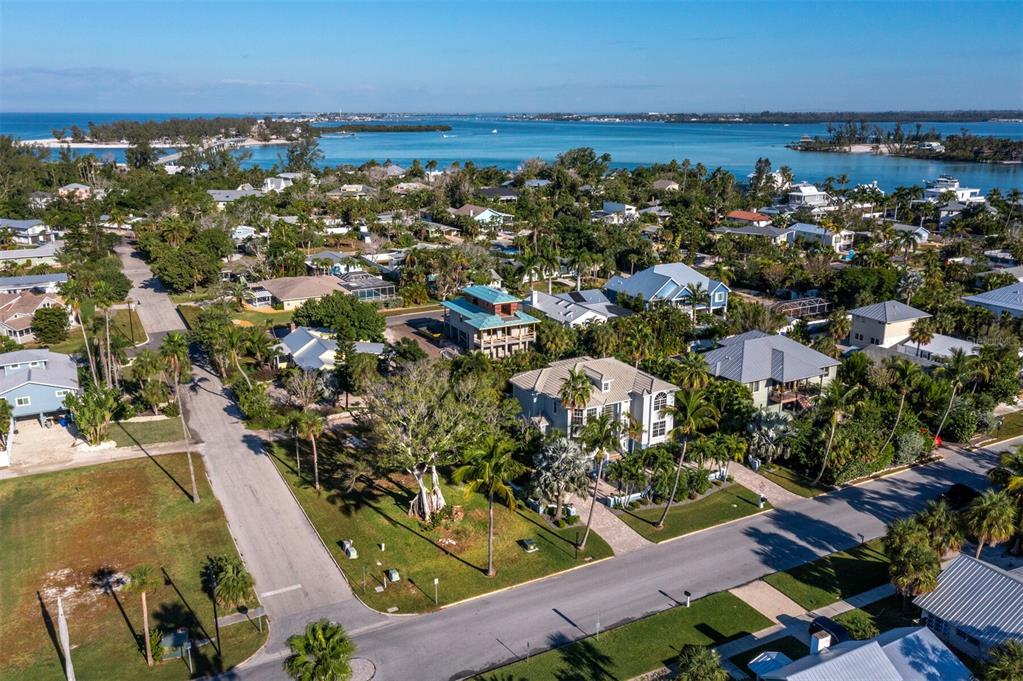 An aerial view shows a coastal neighborhood with houses, palm trees, and a nearby bay — 641 BROADWAY STREET, LONGBOAT KEY, FL