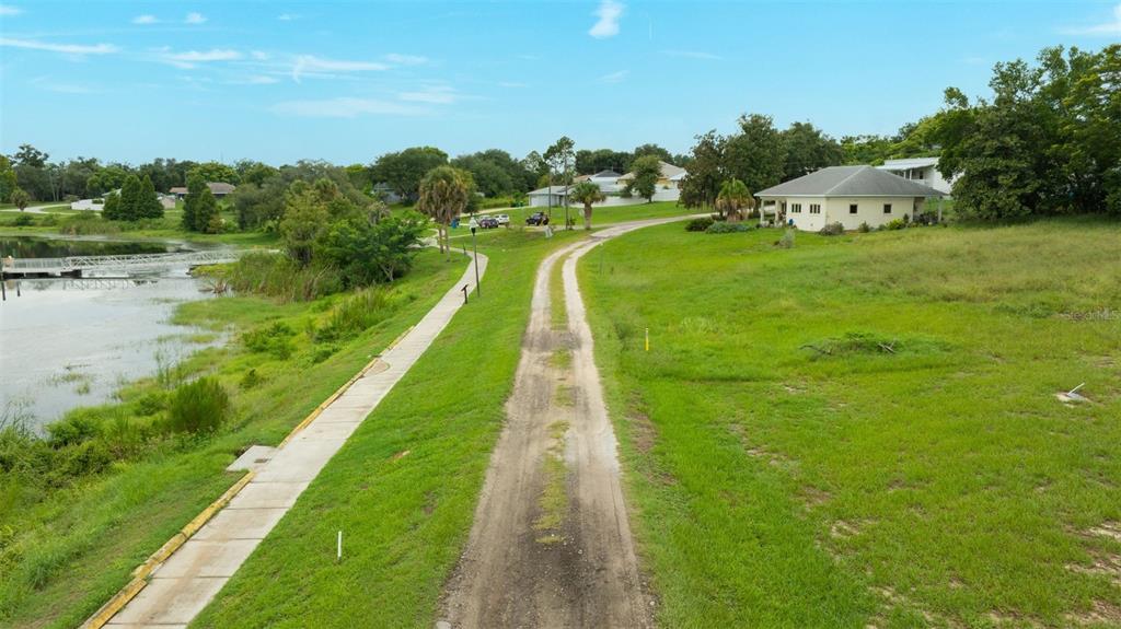An unpaved dirt path runs alongside a concrete sidewalk next to a lake and houses — 0 E LAKE MENZIE BOULEVARD Lot 14, DUNDEE, FL