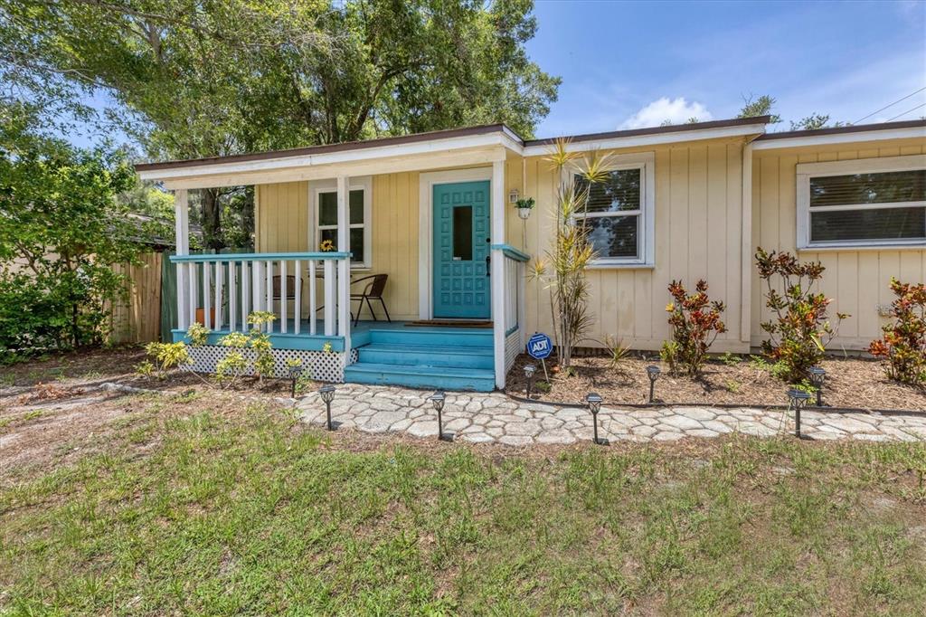 A yellow house features a blue front door, a small porch, and a stone walkway — 900 BEVERLY AVENUE, LARGO, FL