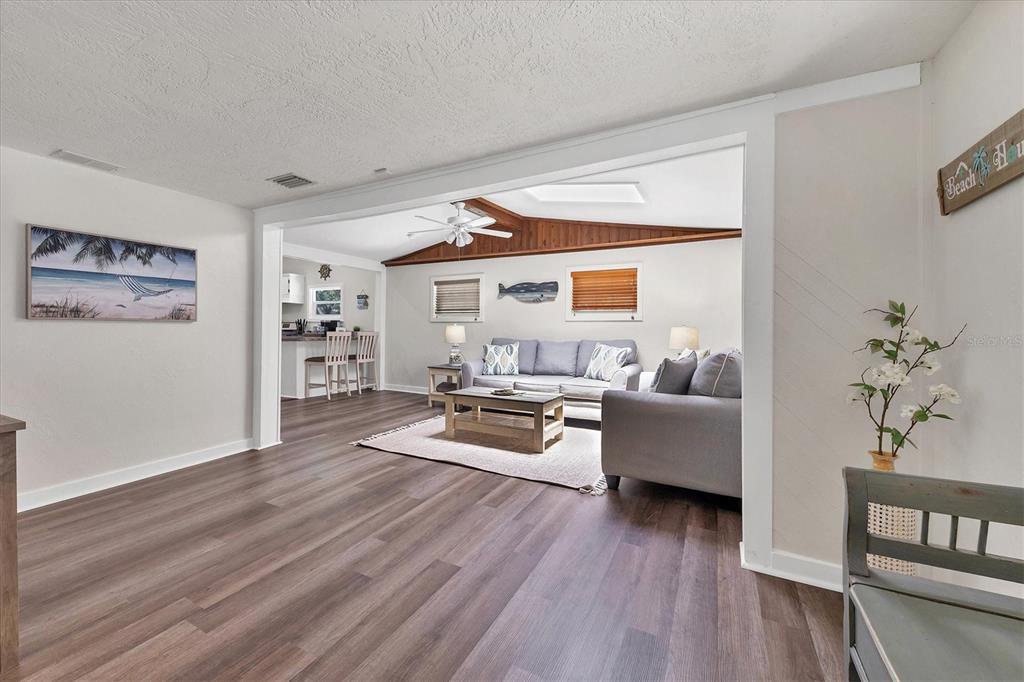 A living room with wood-look flooring opens into a kitchen area with a breakfast bar — 900 BEVERLY AVENUE, LARGO, FL