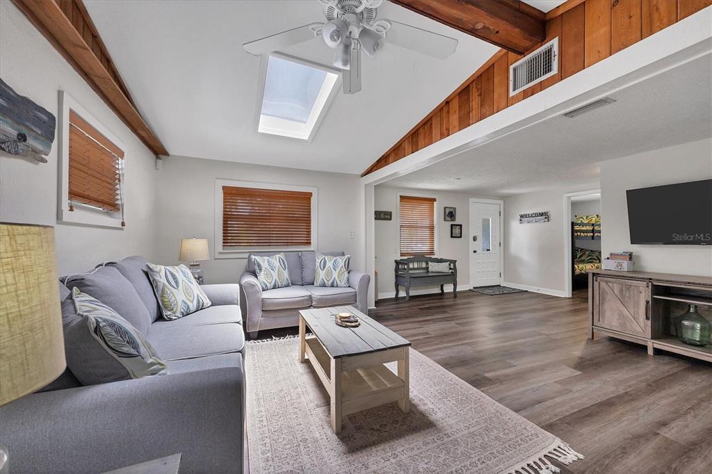 A living room features a vaulted ceiling with a skylight, wood-paneled accents, and gray flooring — 900 BEVERLY AVENUE, LARGO, FL
