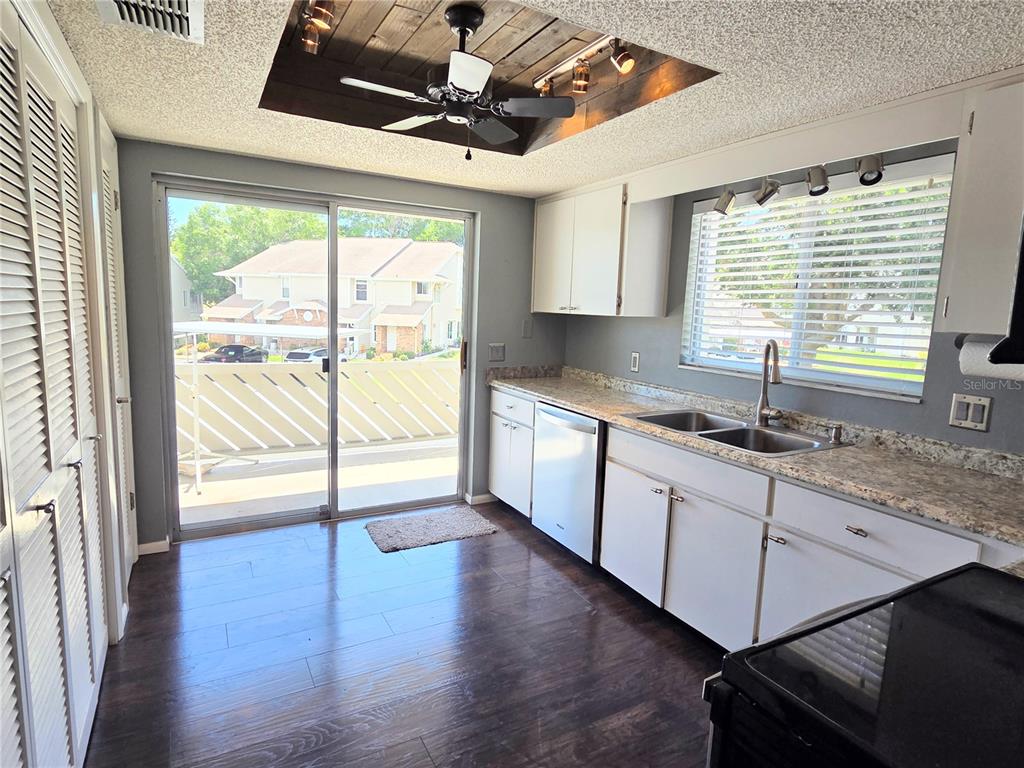 A kitchen with white cabinets, granite countertops, dark wood flooring, and a sliding glass door — 12404 EAGLESWOOD DRIVE UNIT C, HUDSON, FL