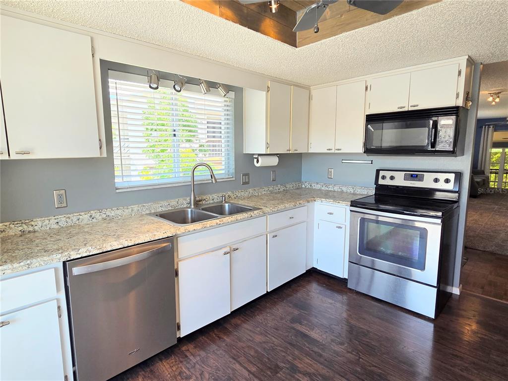 A kitchen features white cabinets, stainless steel appliances, granite countertops, and dark wood flooring — 12404 EAGLESWOOD DRIVE UNIT C, HUDSON, FL