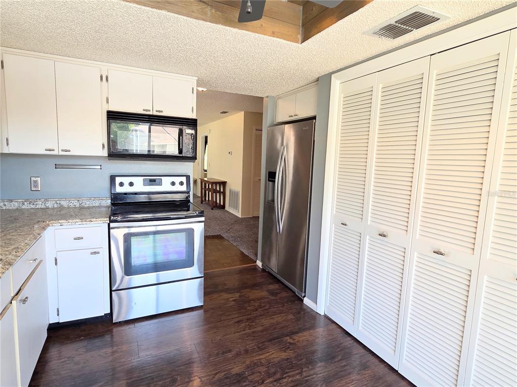 A kitchen featuring white cabinets, stainless steel appliances, granite countertops, and dark wood flooring — 12404 EAGLESWOOD DRIVE UNIT C, HUDSON, FL
